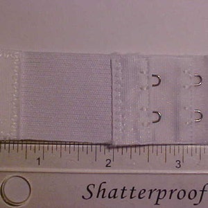 May include: White bra extender with two rows of hooks and eyes. The extender is about 1 inch wide and 3 inches long.