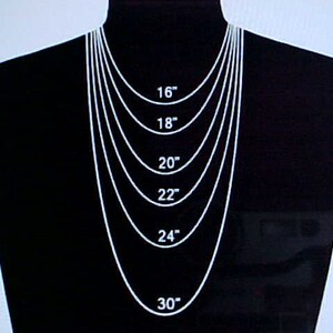 May include: A black mannequin wearing a silver chain necklace with different lengths marked in inches: 16, 18, 20, 22, 24, and 30 inches.