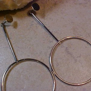 May include: A pair of silver-toned hoop earrings. Each earring features a small, round stud connected to a long, thin bar that leads to a large, circular hoop. The earrings are displayed against a neutral background.