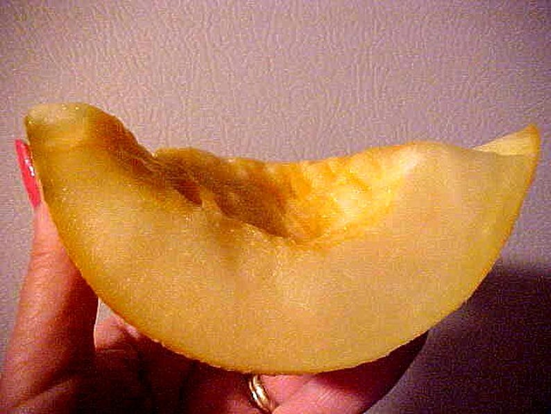 May include: A slice of ripe cantaloupe melon, showcasing a vibrant yellow-orange hue. The melon's flesh is textured, with a slightly rough surface. The image highlights the juicy interior of the fruit, suggesting freshness and a sweet taste.