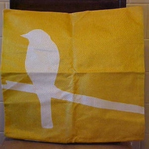May include: A yellow throw pillow with a white silhouette of a bird perched on a branch.