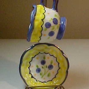 May include: A yellow and blue teacup and saucer set with a floral design. The set is on a gold metal stand.