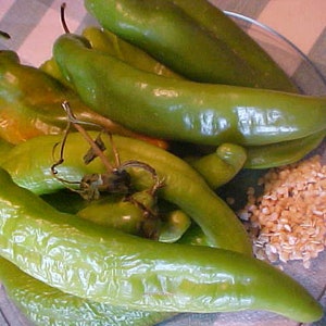 May include: A close-up of a bowl filled with green chili peppers and white grains. The peppers are various sizes and shapes, some are whole and some are cut in half.
