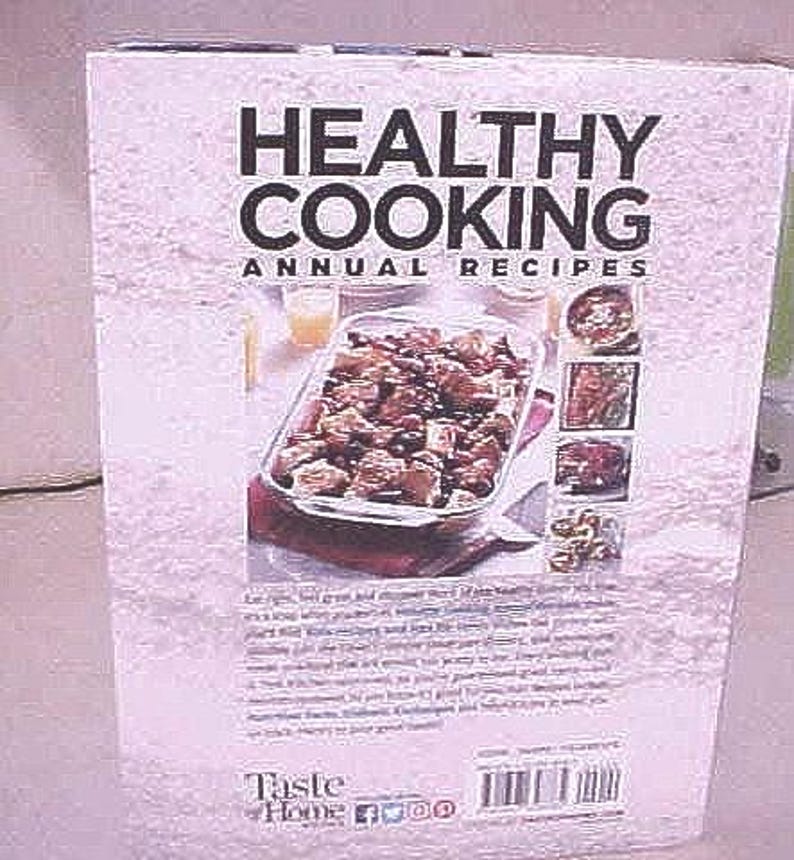 K&ouml;nnte beinhalten: Ein Kochbuch mit dem Titel "Healthy Cooking Annual Recipes" mit helllila Hintergrund. Das Cover zeigt den Titel in gro&szlig;en schwarzen Buchstaben, ein Foto eines Auflaufs und mehrere kleinere Essensbilder. Das Taste of Home-Logo befindet sich unten.