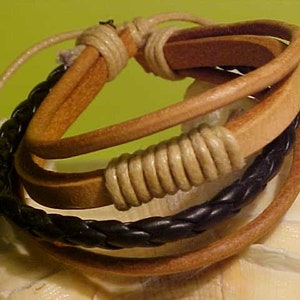 May include: A multi-layered leather bracelet with a braided brown leather strap and a black braided leather strap. The bracelet has a light brown leather strap with a knotted design.