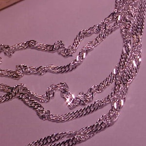 May include: A silver chain necklace with a twisted rope design. The chain is layered and appears to be made of multiple strands.