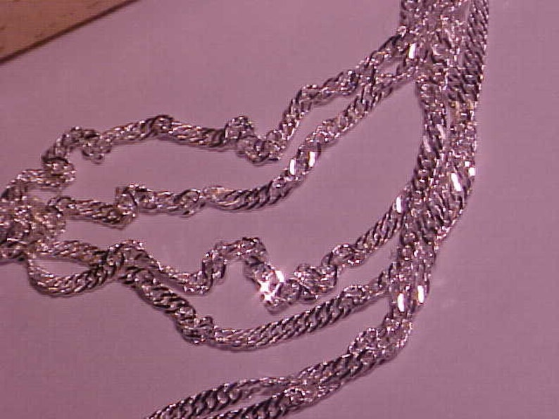May include: A silver chain necklace with a twisted rope design. The chain is layered and appears to be made of multiple strands.