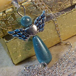 May include: A silver chain necklace with a turquoise and silver angel pendant. The angel has wings and a heart in the center. The necklace is displayed in a gold box.
