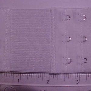 May include: White bra extender with three rows of hooks and eyes. The extender is about 1 inch wide and 3 inches long.