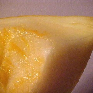May include: Close-up of a wedge of cantaloupe melon. The flesh is a vibrant orange color, with a juicy, glistening texture. The rind is a pale yellow, and the fruit appears fresh and ripe.