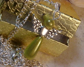 May include: A silver chain necklace with a green glass pendant shaped like a teardrop. The pendant has a silver angel wing design. The necklace is displayed on a gold box with a textured surface.