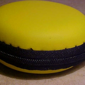 May include: A bright yellow round case with a black zipper and a black trim around the edge.