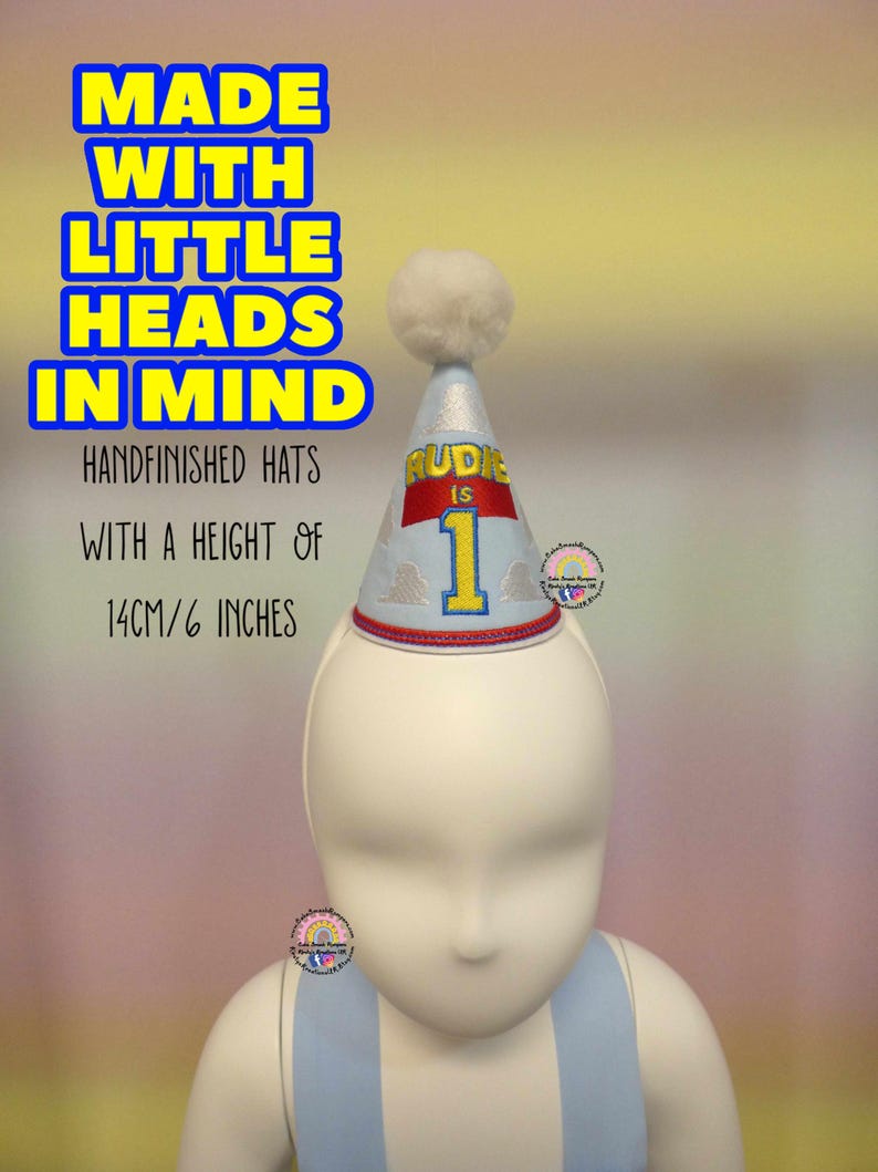 May include: A light blue and silver party hat with a white pom-pom on top. The hat is decorated with the text "RUDIE IS 1" and is 6 inches tall. The text "MADE WITH LITTLE HEADS IN MIND" is also visible.