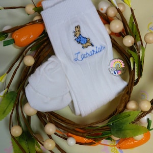 May include: White baby socks with an embroidered Peter Rabbit design and the name "Zachariah" in blue thread.