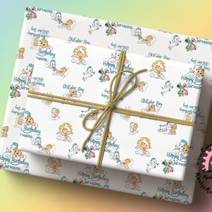 May include: White gift wrap with a repeating pattern of cartoon babies, clouds, and the text "Happy Birthday Jermaine" and "ONEder Boy." The wrapped gift is tied with a brown twine bow.