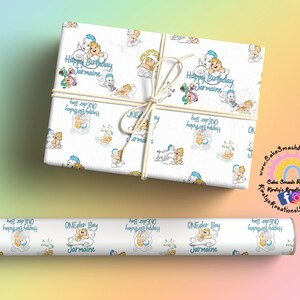 May include: White gift wrap and a roll of wrapping paper featuring a repeating pattern of cartoon characters and the text "Happy Birthday Jermaine" in blue. The gift is tied with twine.