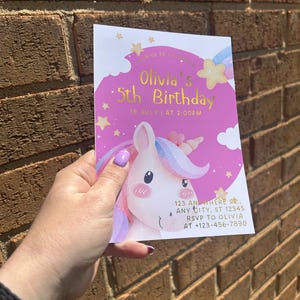 Może przedstawiać: R&oacute;żowo-białe zaproszenie urodzinowe z ilustracją jednorożca. Na zaproszeniu widnieje napis "Olivia's 5th Birthday" z datą i godziną. Zawiera r&oacute;wnież adres i informacje RSVP.