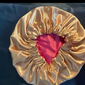 May include: A gold satin sleep cap with a pink satin lining. The cap is gathered at the top and has a drawstring.