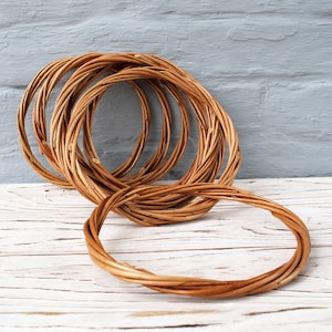 May include: A set of six brown wicker wreath rings, stacked on top of each other, on a white wooden surface.