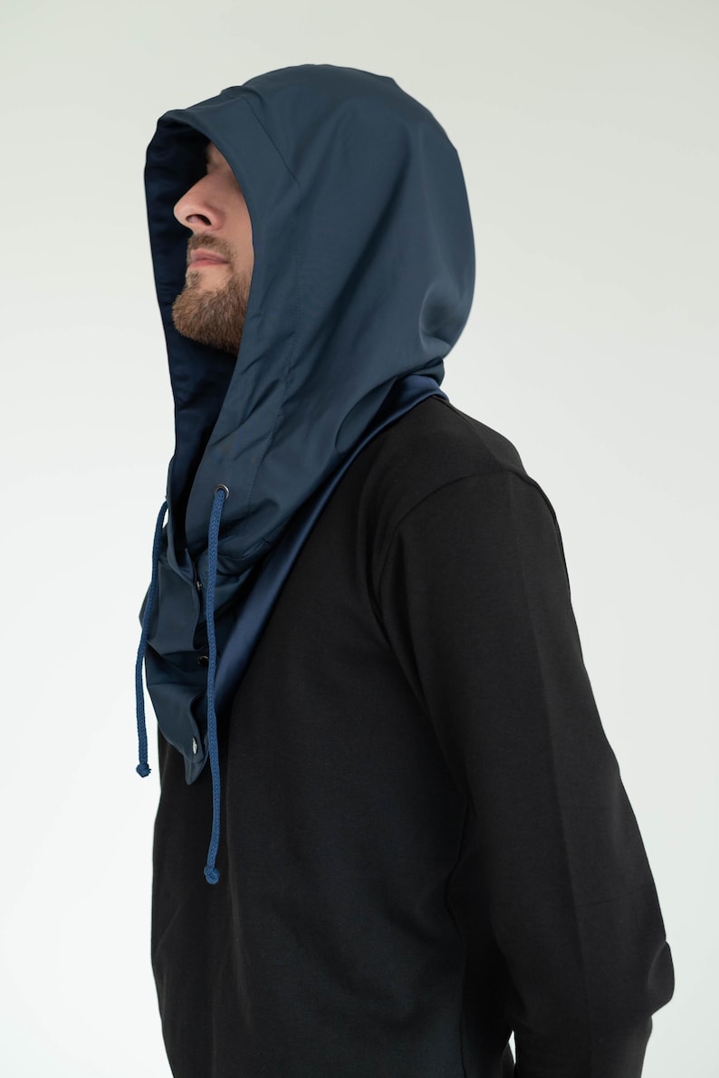 May include: A dark blue hood with a smooth, matte finish and a matching drawstring. The hood features a structured design that covers the head and neck, with metal eyelets for the drawstring and a button closure at the front neck area.