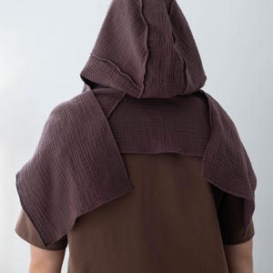 May include: A brown hooded cape and matching short-sleeved shirt. The hood and cape are made of a textured, dark mauve fabric, with visible stitching details. The shirt is a solid, medium brown color, creating a layered effect.