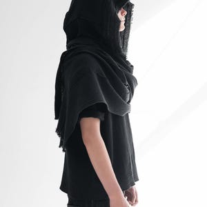 May include: A black hooded scarf and top. The hood is draped over the shoulders, and the top has short sleeves. The fabric appears to be a lightweight, textured material. The person is wearing black jeans.