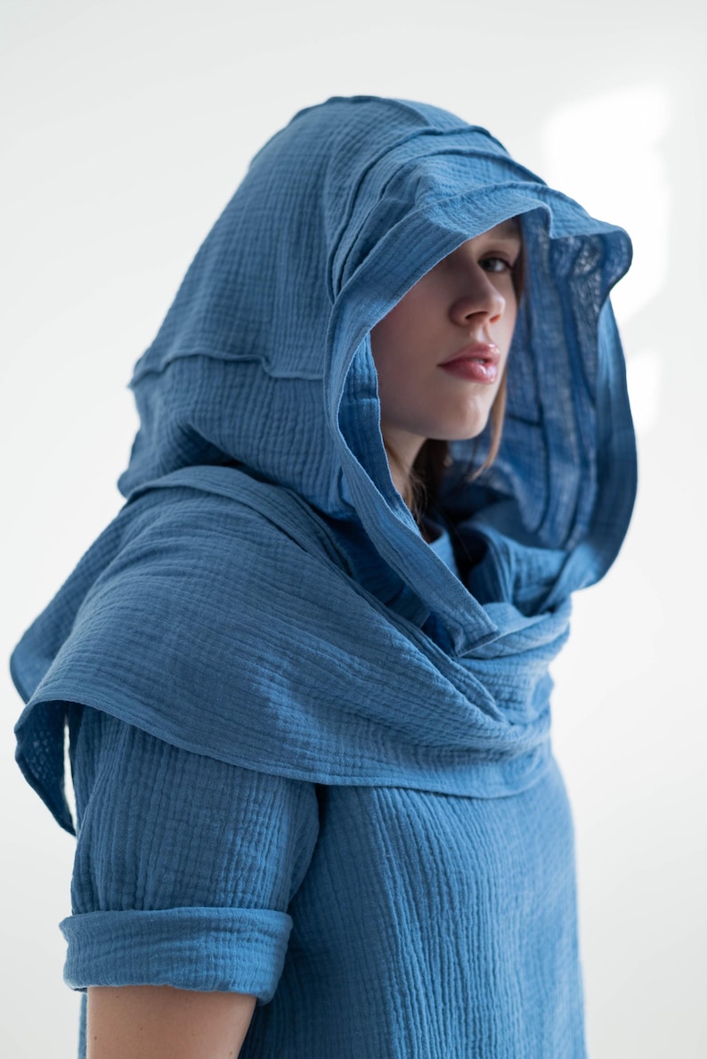 May include: A blue hooded garment with a layered design. The hood is draped around the shoulders and neck, and the sleeves are rolled up. The fabric has a textured appearance.