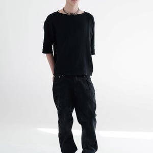 May include: A person wearing a black beanie, a black long-sleeve shirt, and black jeans. The shirt has a boat neck and the jeans are slightly baggy. The person is also wearing a necklace and silver trainers.