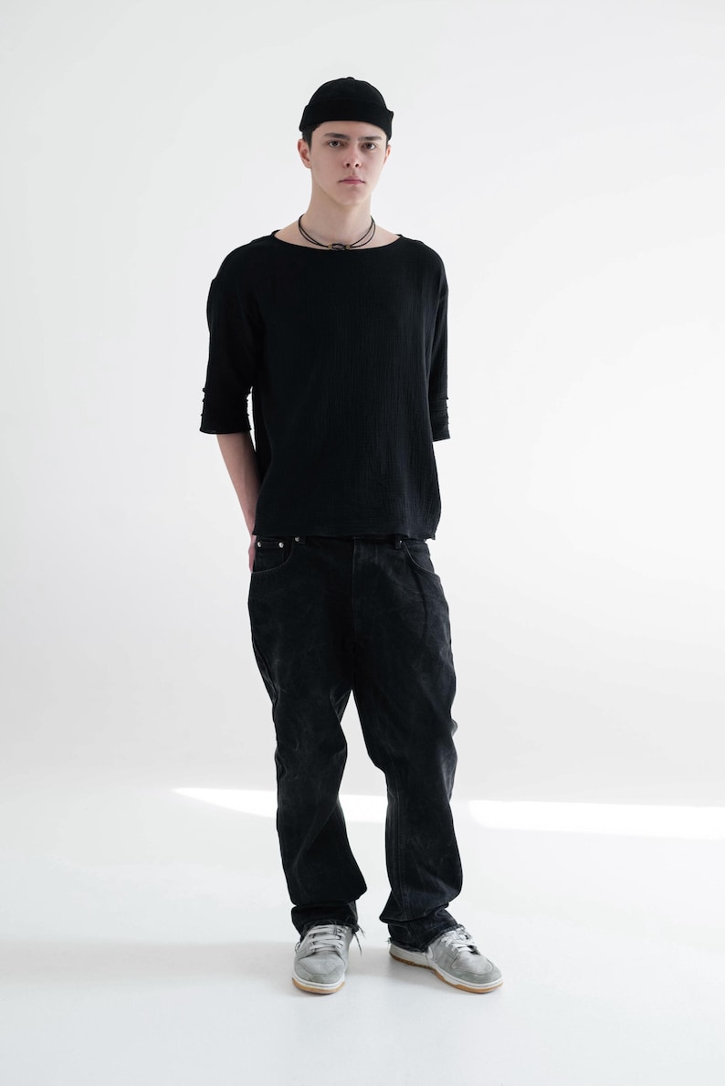 May include: A person wearing a black beanie, a black long-sleeve shirt, and black jeans. The shirt has a boat neck and the jeans are slightly baggy. The person is also wearing a necklace and silver trainers.