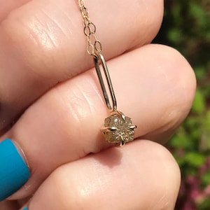 May include: A delicate gold chain necklace with a small, raw diamond pendant. The diamond is a light brown color and has a rough, natural texture.