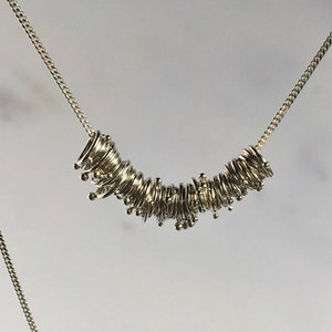 Può includere: Una collana d'argento con un gruppo di piccoli anelli interconnessi che formano una forma curva.
