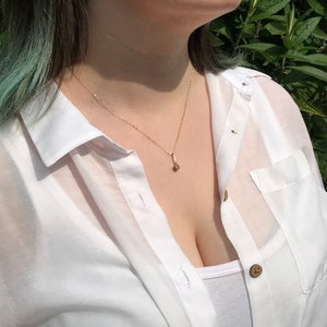 May include: A woman wearing a white button-down shirt with a gold chain necklace and a small pendant.
