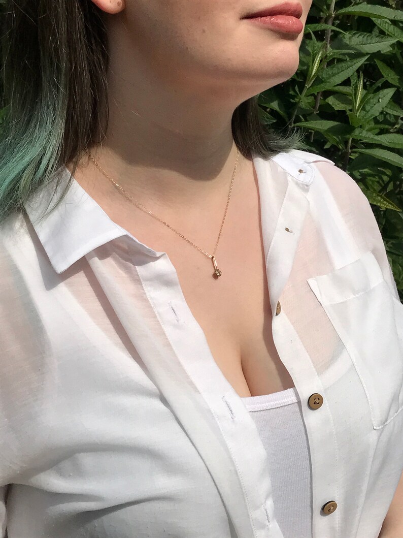 May include: A woman wearing a white button-down shirt with a gold chain necklace and a small pendant.
