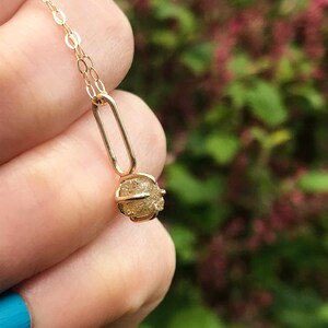 May include: A gold chain necklace with a small, round, raw diamond pendant. The diamond is set in a gold cage.