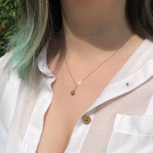 May include: A gold chain necklace with a small, round pendant. The necklace is worn by a person with light green hair and a white button-down shirt.