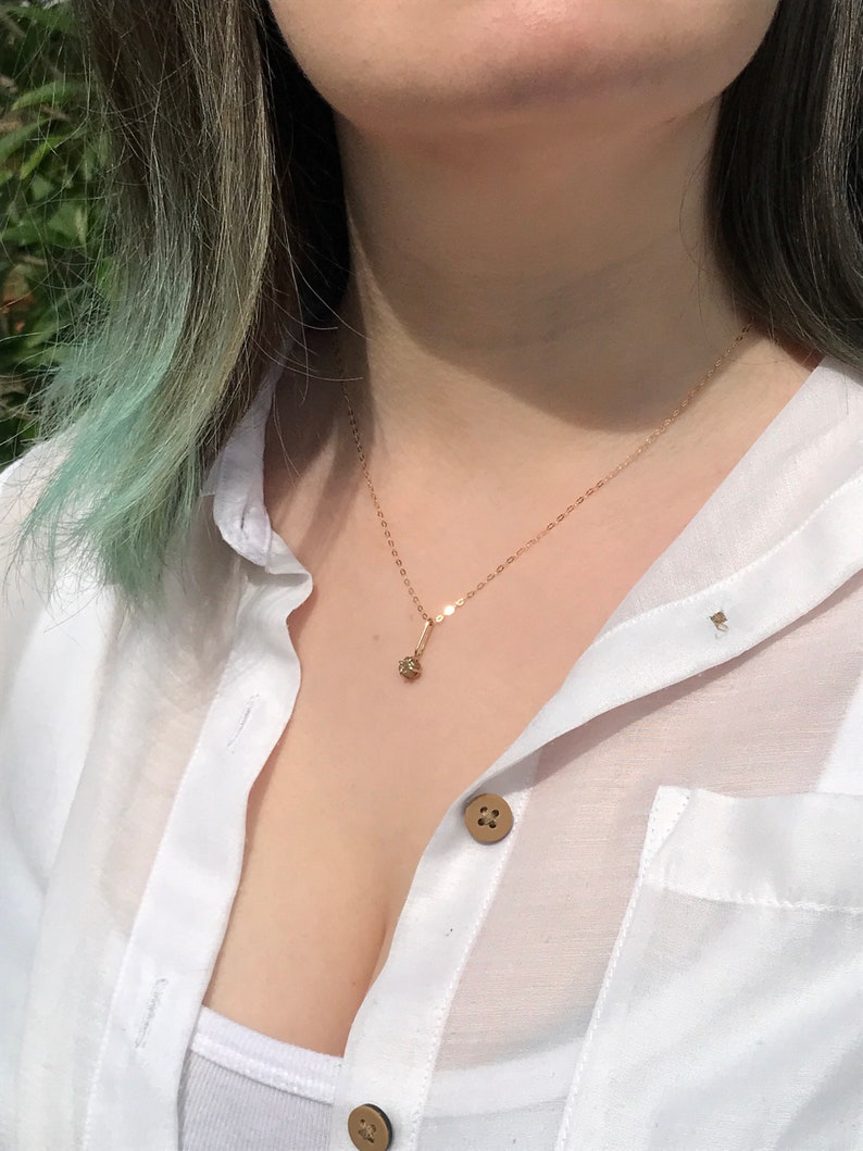 May include: A gold chain necklace with a small, round pendant. The necklace is worn by a person with light green hair and a white button-down shirt.