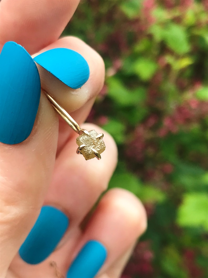 May include: A delicate gold ring with a small, raw, light brown diamond. The diamond is set in a simple, four-prong setting.