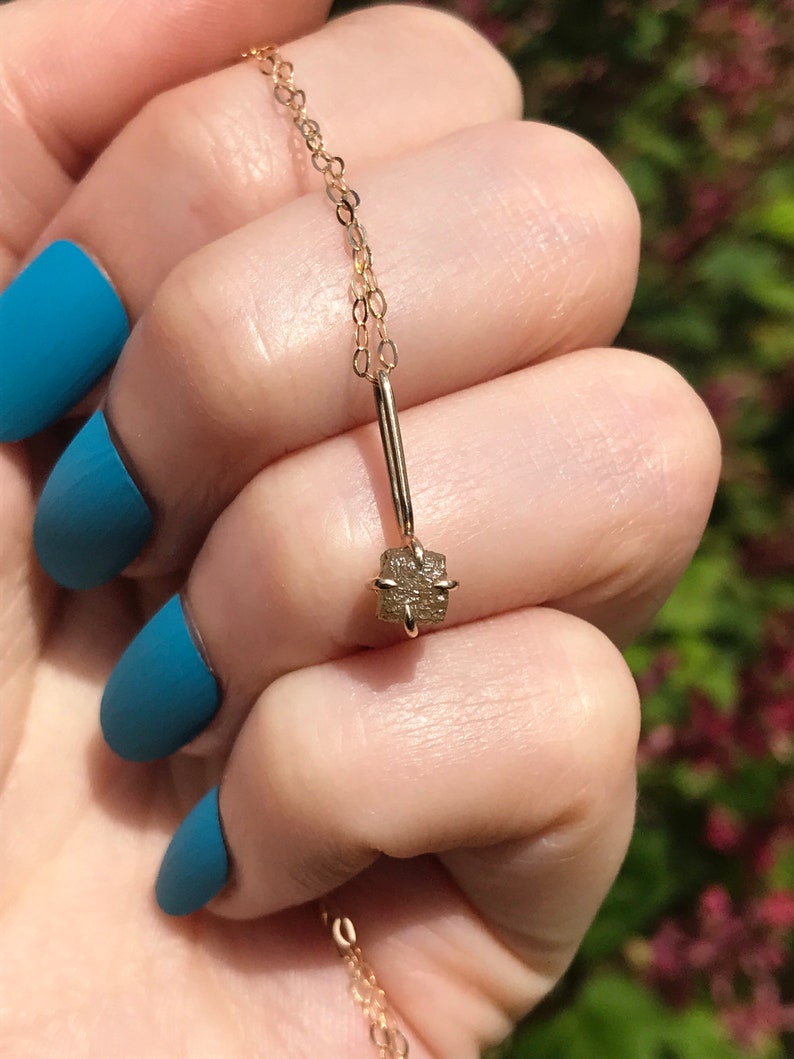 May include: A delicate gold chain necklace with a small, square-shaped, rough-cut diamond pendant.
