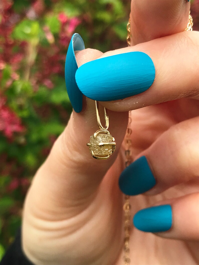May include: A gold necklace with a small, rough, yellow gemstone pendant. The pendant is shaped like a small, irregular cube.