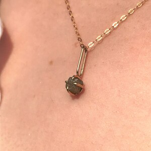 May include: A gold chain necklace with a small, rough, gray diamond pendant.