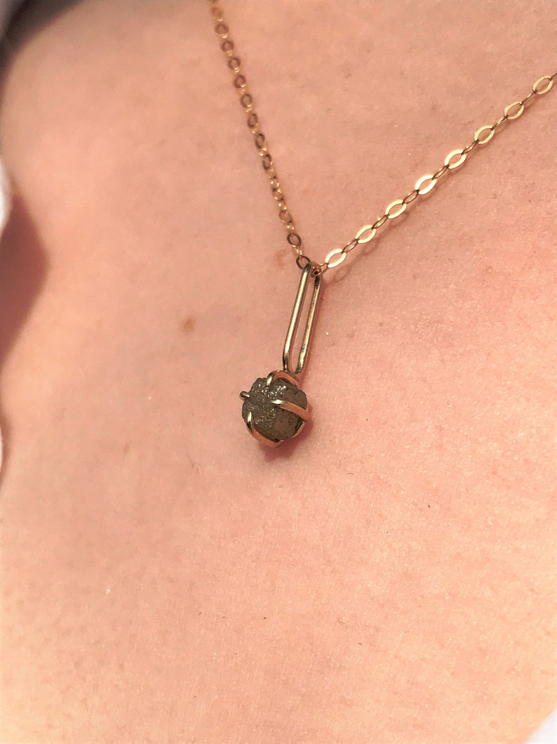 May include: A gold chain necklace with a small, rough, gray diamond pendant.