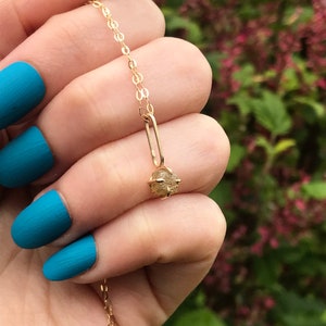 May include: A gold chain necklace with a small, raw, light brown diamond pendant.