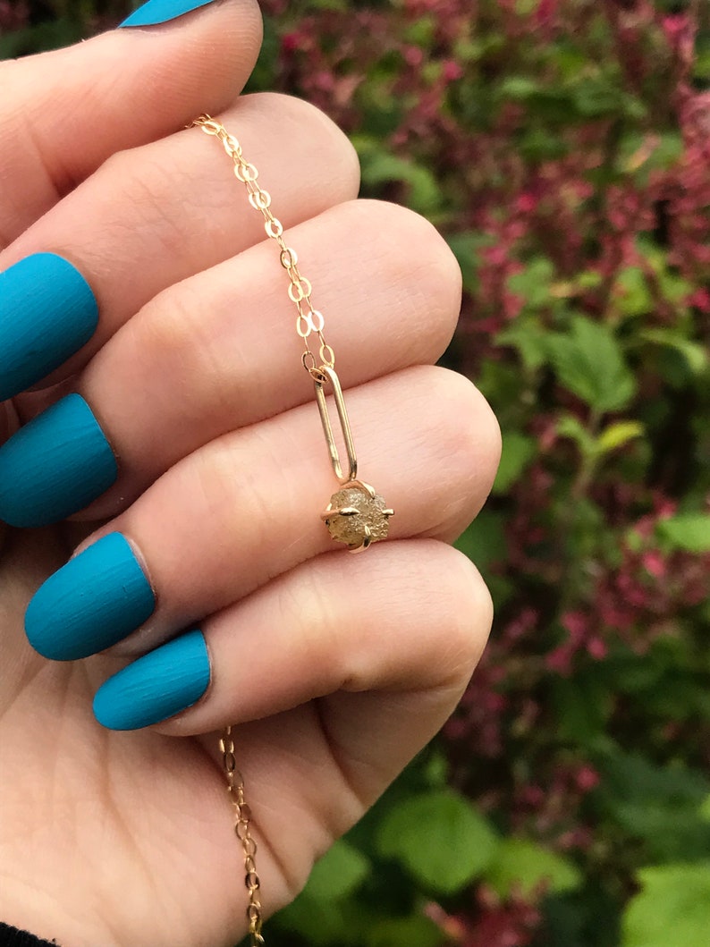 May include: A gold chain necklace with a small, raw, light brown diamond pendant.