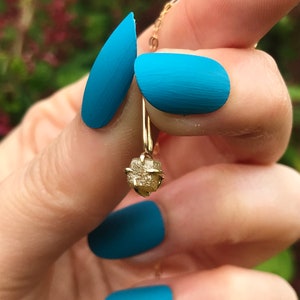 May include: A gold pendant necklace with a rough, raw diamond-shaped stone. The necklace is hanging from a person's finger with blue nail polish.