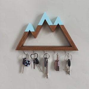 May include: A wooden key holder shaped like a mountain range with a light blue painted top. The holder has five hooks for hanging keys, and there are five keys and a small harmonica hanging from the hooks.