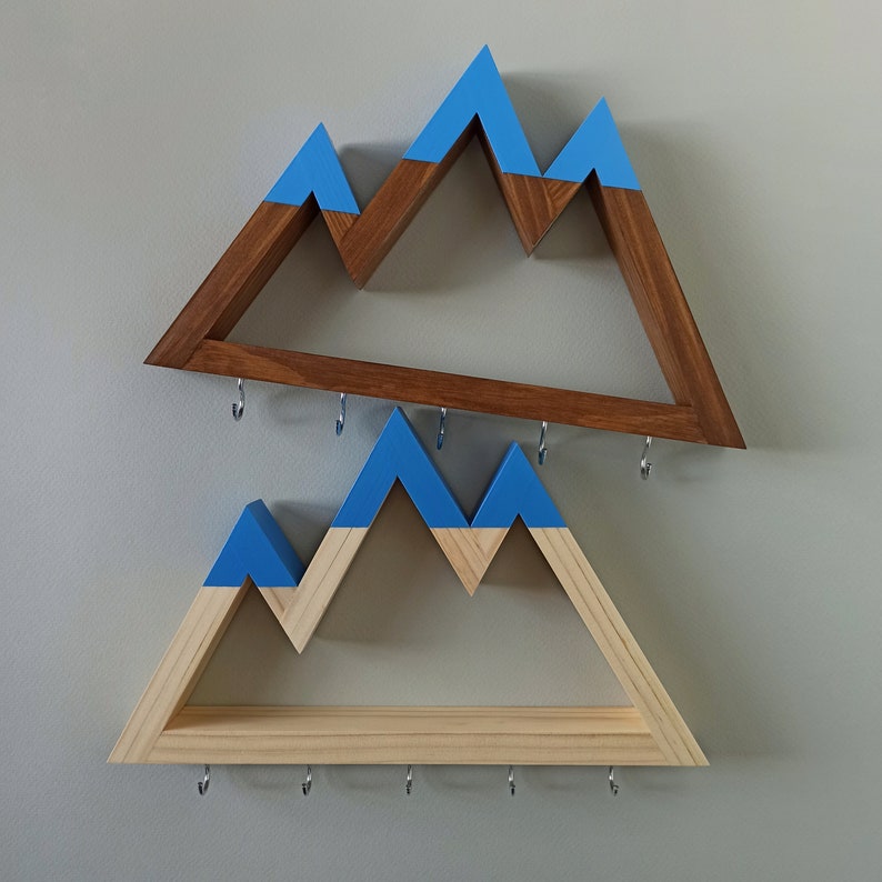 May include: Two wooden mountain-shaped shelves with blue painted peaks. The top shelf is brown wood and the bottom shelf is natural wood. Both shelves have hooks for hanging items.