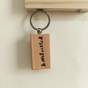 May include: A rectangular light-colored wooden keychain featuring a silver metal ring attached to the top. The wood block has the word "faithful" burned into the surface in a vertical orientation using a dark, textured script font.
