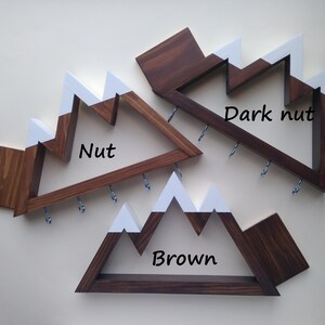 May include: Three wooden mountain-shaped key racks with white painted peaks. The racks are stained in three different shades of brown: "Nut", "Brown", and "Dark Nut".