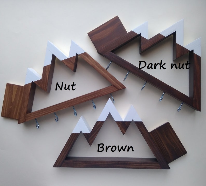 May include: Three wooden mountain-shaped key racks with white painted peaks. The racks are stained in three different shades of brown: "Nut", "Brown", and "Dark Nut".