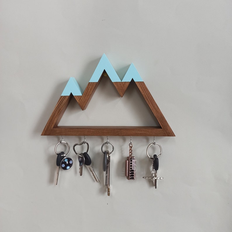 May include: A wooden key holder shaped like a mountain range with a light blue painted top. The holder has five hooks for hanging keys, and there are five keys and a small harmonica hanging from the hooks.